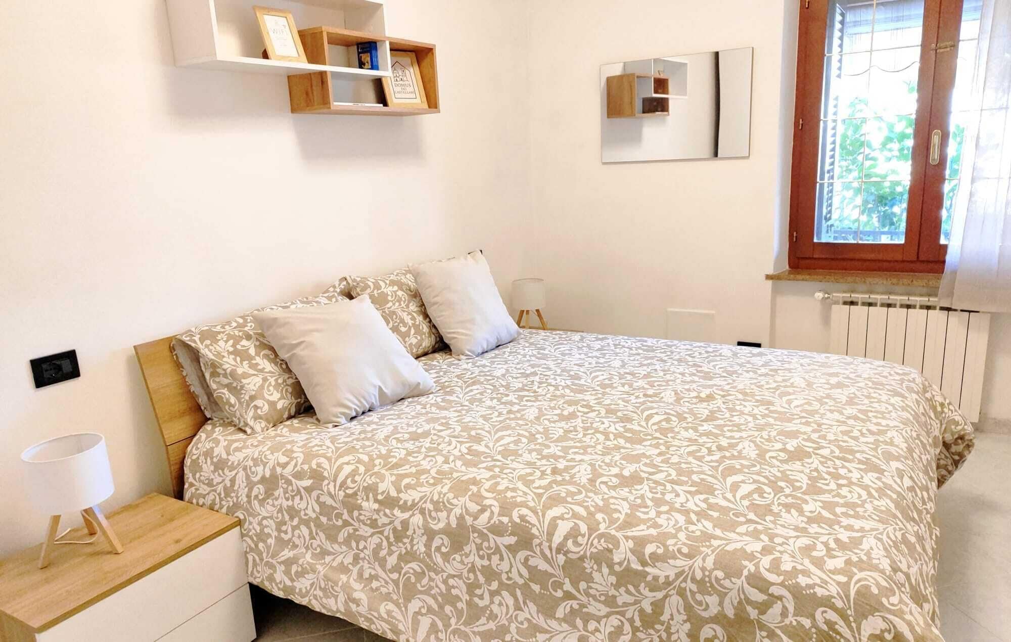 Una camera da letto con un letto, comodini, una mensola con quadri incorniciati, uno specchio e una finestra vista verde.