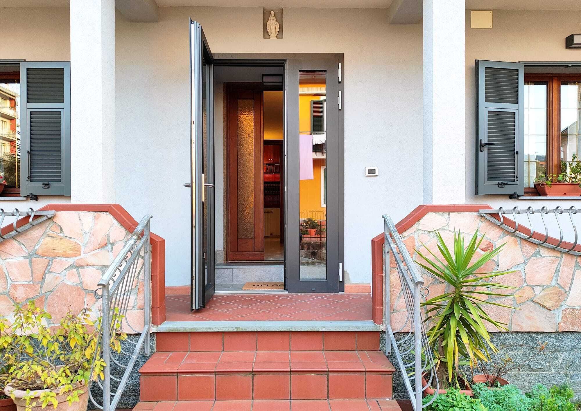 Une entrée d’immeuble avec un escalier en pierre, une rampe métallique et une porte donnant sur un espace intérieur.