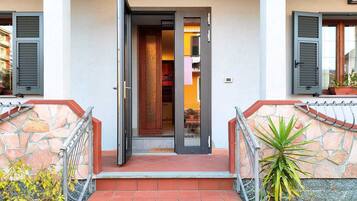 Une entrée d’immeuble avec un escalier en pierre, une rampe métallique et une porte donnant sur un espace intérieur.