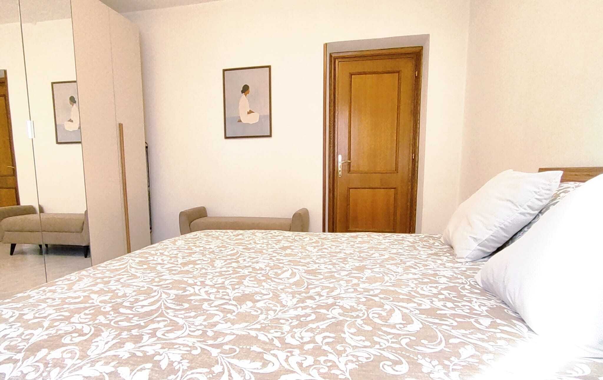 A bedroom with a bed, a chair, a wardrobe, and a door.