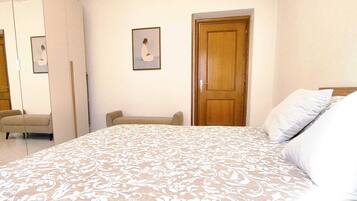 A bedroom with a bed, a chair, a wardrobe, and a door.