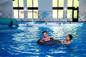 En indendørs swimmingpool med krystalklart vand, et springbræt og en flisebeklædt væg med vinduer.