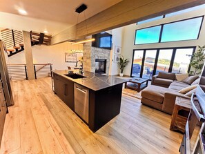 A modern kitchen with a central island, a dining area with a sofa, and a staircase leading to an upper level.