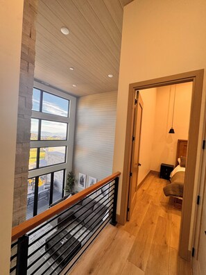 Un intérieur moderne avec un escalier en bois, une vue dégagée grâce à de grandes fenêtres et une porte donnant sur une autre pièce.