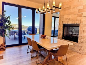 A modern dining area with a large table, chairs, a fireplace, and a view of the outdoors.