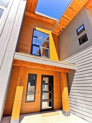 A modern two-story building with a prominent wooden facade, a balcony, and a clear sky above.