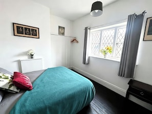 Un dormitorio con cama, mesita de noche, ventana con cortinas e imágenes colgadas en la pared.