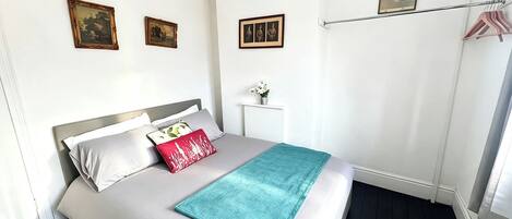 A neatly arranged bedroom with a bed, pillows, a bedside table with a vase, and a wall-mounted picture.