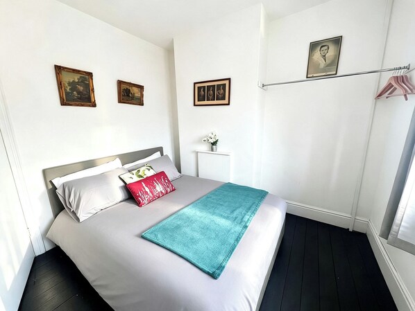 A neatly arranged bedroom with a bed, pillows, a bedside table with a vase, and a wall-mounted picture.