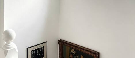 A staircase with a white balustrade, a framed black-and-white photograph, and a framed painting of flowers.