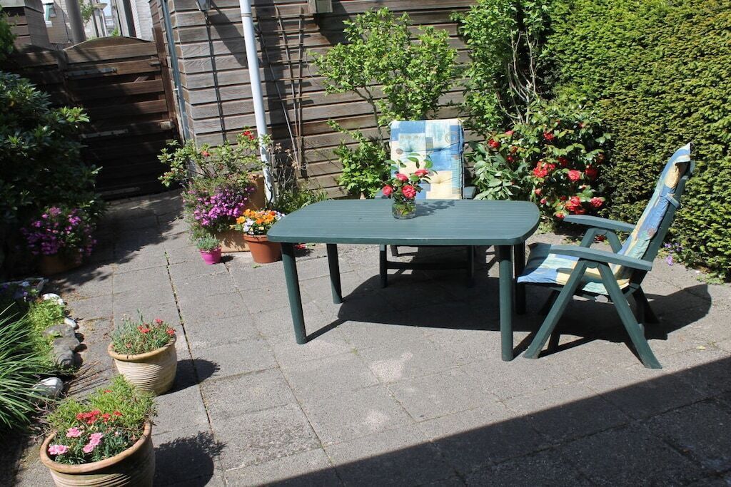 An outdoor patio with a table and chair, surrounded by potted plants and flowers.