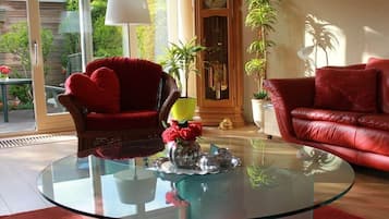 Un salon avec une table basse en verre, des fauteuils rouges et des plantes en pot.