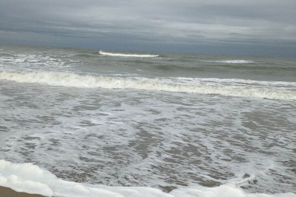 Une plage où les vagues se brisent près du rivage, un ciel nuageux et un horizon lointain.