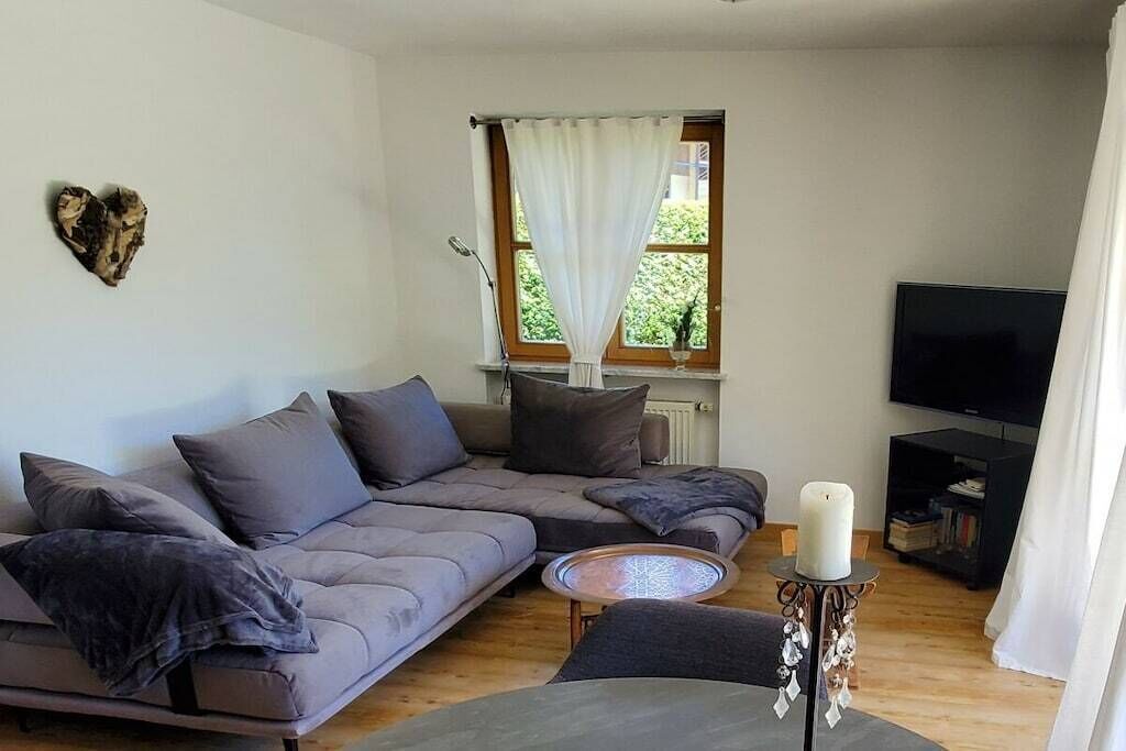 A modern living room with a sectional sofa, a small round coffee table, a flat-screen TV, and a window with curtains.