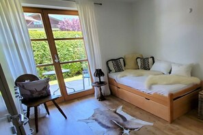 Ein Schlafzimmer mit einem Bett, einem Sessel, einem kleinen Tisch und Blick ins Freie.