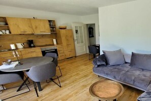 Eine moderne Küche mit Holzausbau, einem Esstisch mit Stühlen und einem grauen Sofa im Wohnbereich.