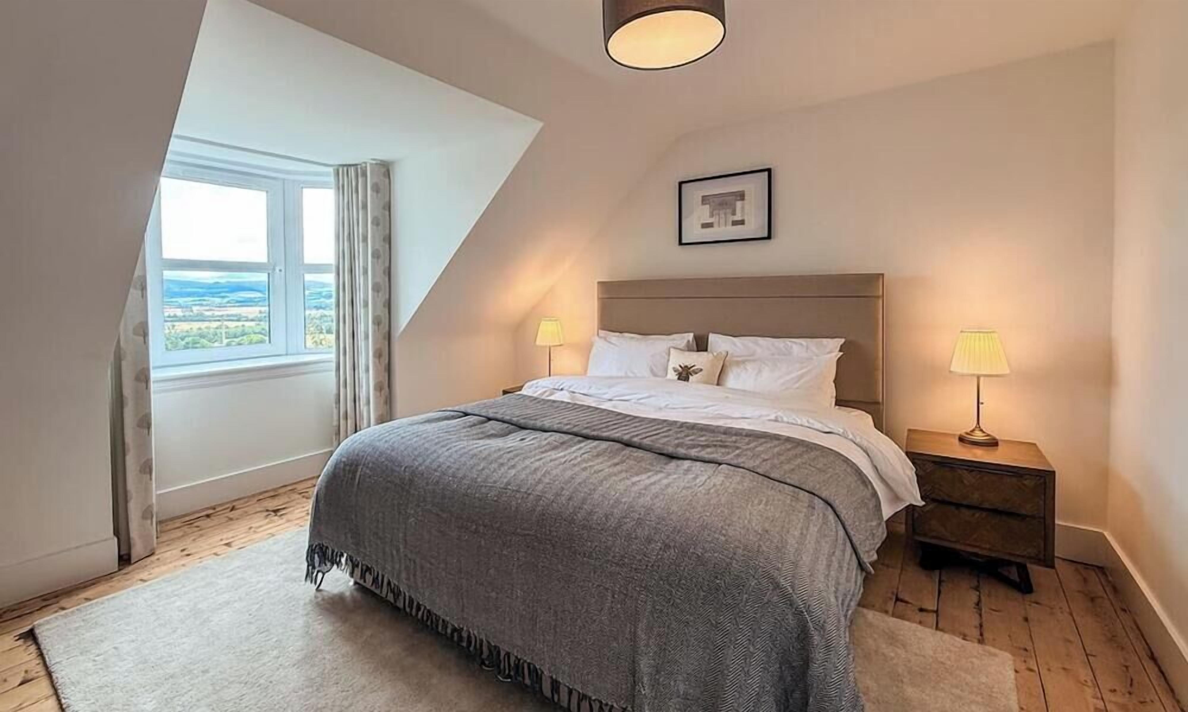 Un dormitorio con cama, dos lámparas de noche, un cuadro en la pared y una ventana con cortinas.