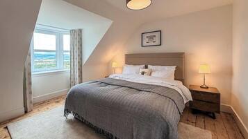 Un dormitorio con cama, dos lámparas de noche, un cuadro en la pared y una ventana con cortinas.