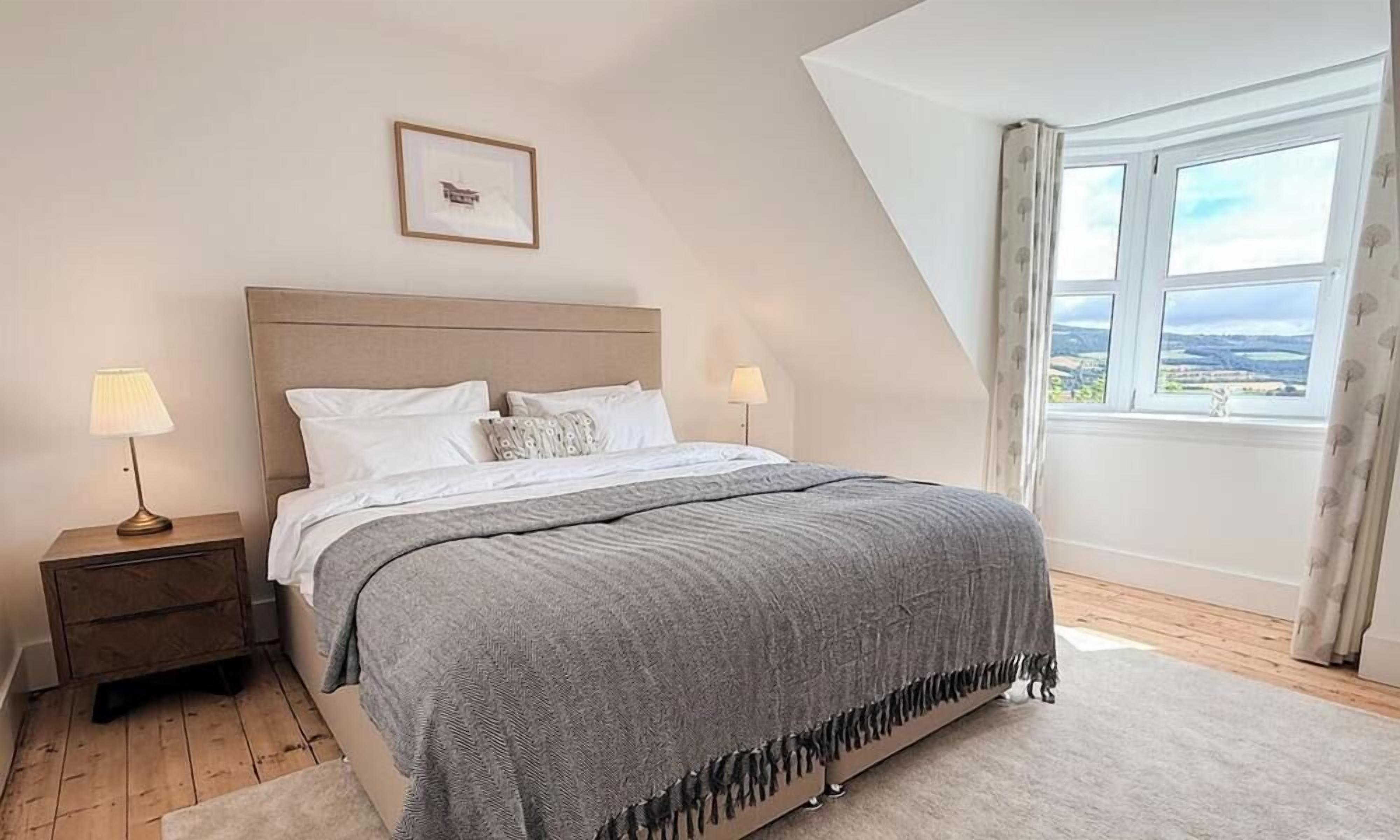 A bedroom with a bed, nightstands, a window with curtains, and a framed picture on the wall.