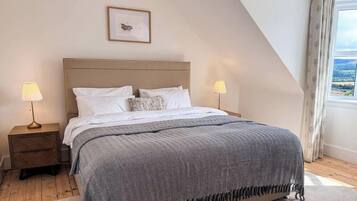 A bedroom with a large bed, two bedside tables, a framed picture on the wall, and a window with curtains.