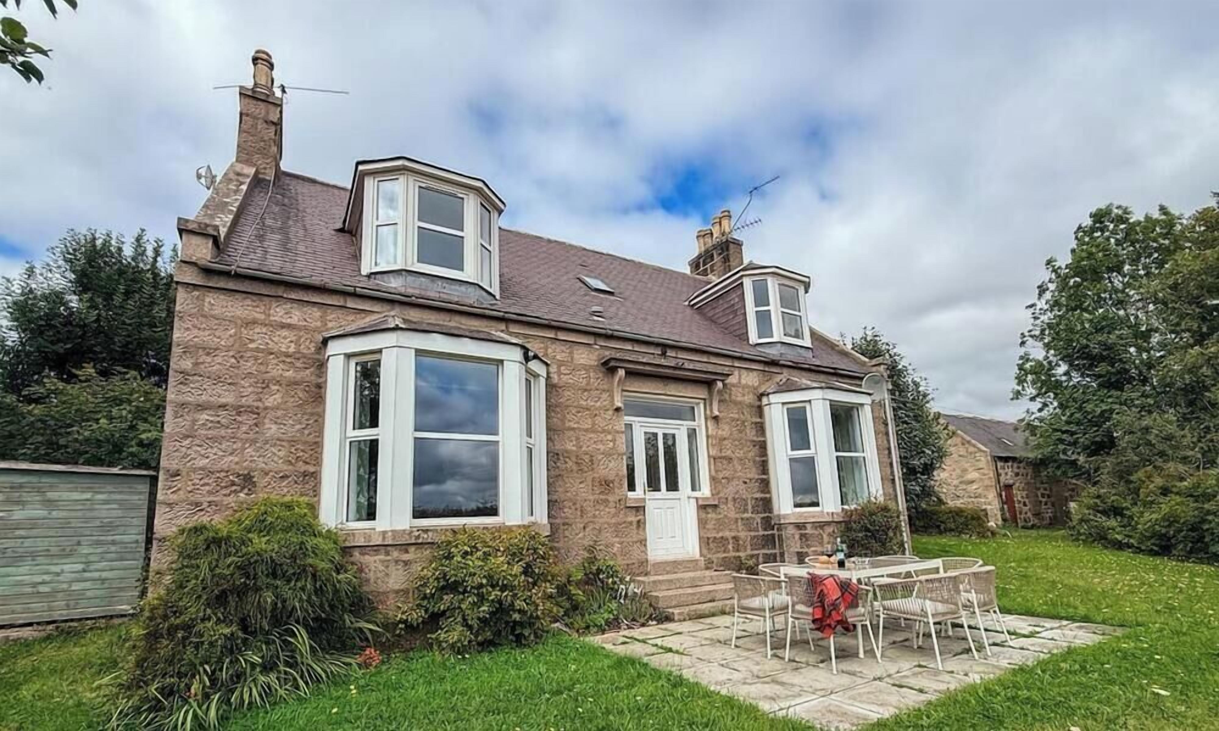 A two-story stone house with a front garden and a patio area.