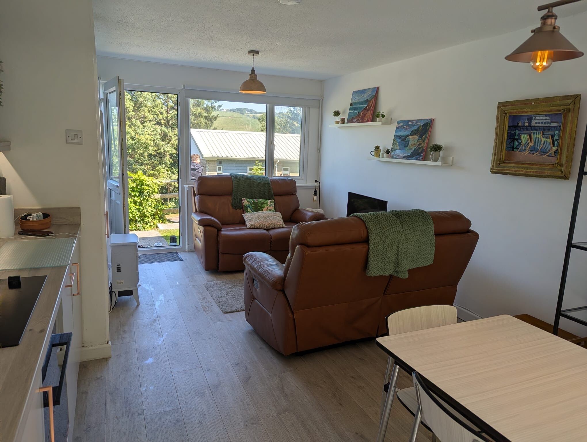 Una sala de estar moderna con un sofá de cuero marrón, una mesa de comedor y un ventanal con vistas al exterior.