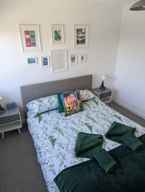 A neatly made bed with a floral bedspread, a pillow with a cityscape design, and a framed quote on the wall. - Sea Holly, stylish home close to lovely beach (Pembroke)