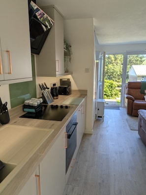 A modern kitchen with a central island, a dining area with a sofa, and a view of greenery outside. - Sea Holly, stylish home close to lovely beach (Pembroke)