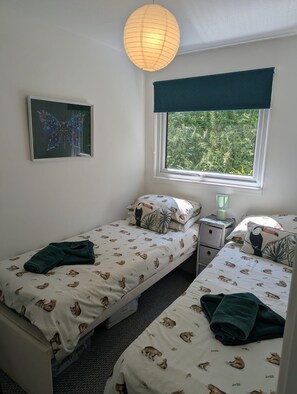 Een slaapkamer met twee eenpersoonsbedden, een raam met uitzicht op groen, een wandlamp en een afbeelding van een vlinder.