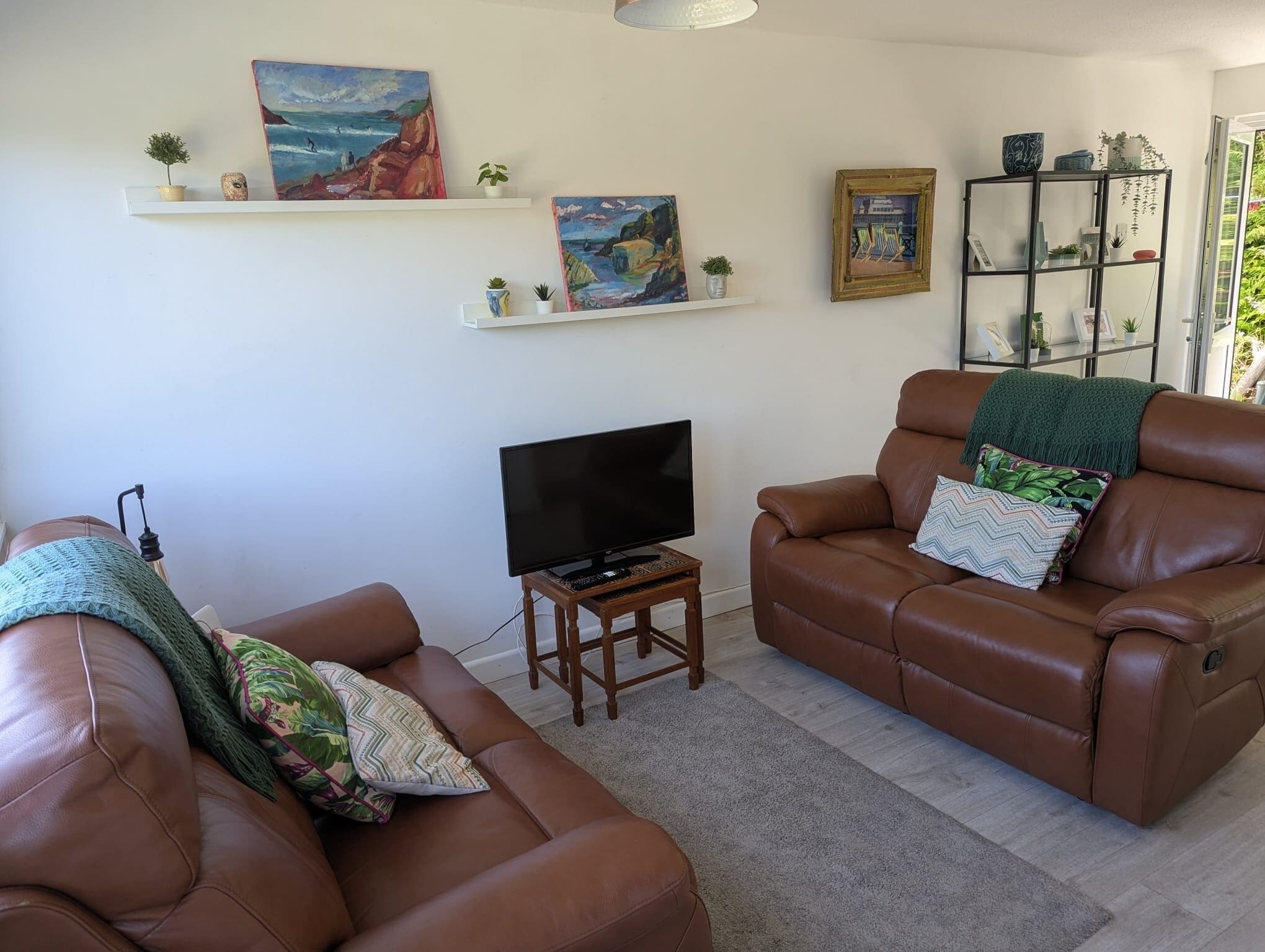 Un salon avec deux canapés en cuir marron, un téléviseur posé sur un meuble en bois et des œuvres d’art accrochées aux murs.