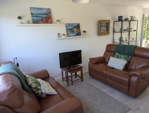Ein Wohnzimmer mit zwei braunen Ledersofas, einem Fernseher auf einem Holzboden und Kunstwerken an den Wänden.