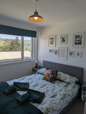 A bedroom with a bed, a window with a view, a bedside table, and wall art. - Sea Holly, stylish home close to lovely beach (Pembroke)