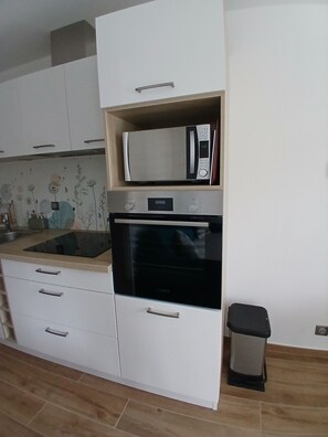 A kitchen with white cabinets, a microwave, an oven, and a trash bin. - 3-Person "Gite Étoiles" (BISCARROSSE PLAGE)