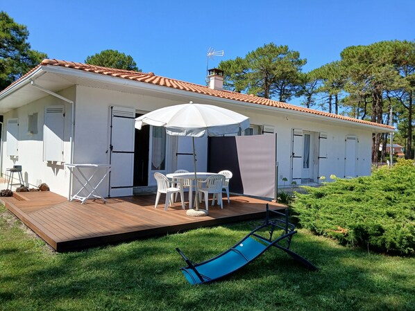 A white building with a tiled roof, a wooden deck, a table with chairs, and a blue lounge chair. - 3-Person "Gite Étoiles" (BISCARROSSE PLAGE)