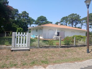 A white building with a red-tiled roof, a fenced yard, and a bench. - 3-Person "Gite Étoiles" (BISCARROSSE PLAGE)