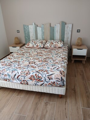 A bed with a floral-patterned duvet, two bedside tables with woven baskets, and a wall with vertical wooden panels. - 3-Person "Gite Étoiles" (BISCARROSSE PLAGE)