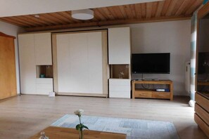 A room with a sliding door, a flat-screen TV on a wooden stand, and a small table with a vase. - Panorama with indoor swimming pool (Hauzenberg)