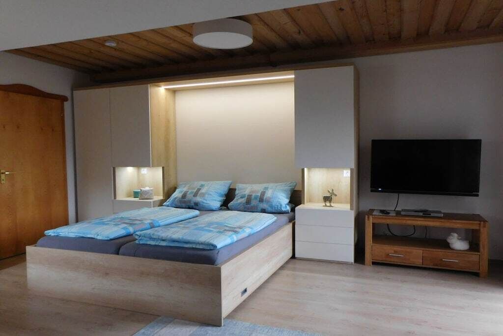 A modern bedroom with a bed, bedside tables, a TV, and a wooden ceiling.