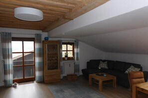 A cozy living room with a wooden ceiling, a black sofa, a wooden coffee table, and a window with curtains. - Panorama with indoor swimming pool (Hauzenberg)
