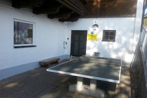 Et udendørs ping pong-bord opstillet foran en hvid væg med en dør og et vindue.