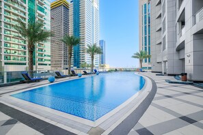 A swimming pool with lounge chairs and palm trees, surrounded by high-rise buildings. - Stayshort - Stylish 2-bedroom Escape in Dubai Marina for 4 Guests (Dubai)