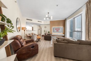 A modern living room with leather sofas, a dining area, and a large window with a view of the city. - Stayshort - Stylish 2-bedroom Escape in Dubai Marina for 4 Guests (Dubai)