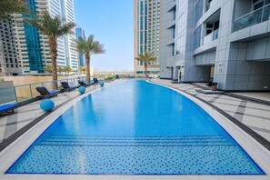 A swimming pool with lounge chairs and palm trees, surrounded by high-rise buildings. - Stayshort - Stylish 2-bedroom Escape in Dubai Marina for 4 Guests (Dubai)