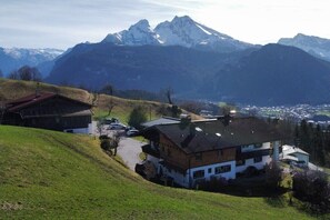 A house with a sloped roof, surrounded by a green hillside, with a mountain range in the background. - Kranvogllehen holiday farm (Schönau am Königssee)