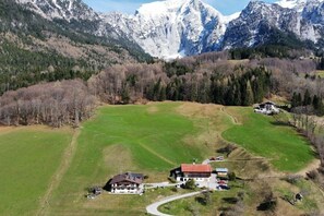 Ein ländliches Anwesen mit einem großen grünen Feld, einem Gebäude mit rotem Dach und einer Bergkette im Hintergrund.