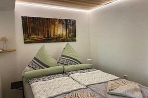 A bedroom with a bed, pillows, a wall-mounted painting, and a bedside table with a lamp. - Holiday apartment with 1 bedroom (Baiersbronn)