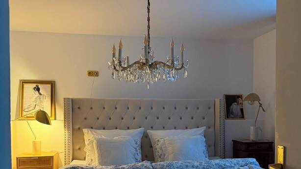 A bedroom with a large bed, a chandelier, a bedside table, a lamp, and a framed picture on the wall. - Stylish living in a 95-square-meter apartment with a great view from the garden (Bad Laasphe)