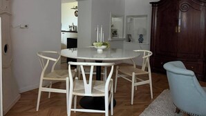 A dining area with a round table and four chairs, a wooden cabinet, and a blue armchair. - Stylish living in a 95-square-meter apartment with a great view from the garden (Bad Laasphe)