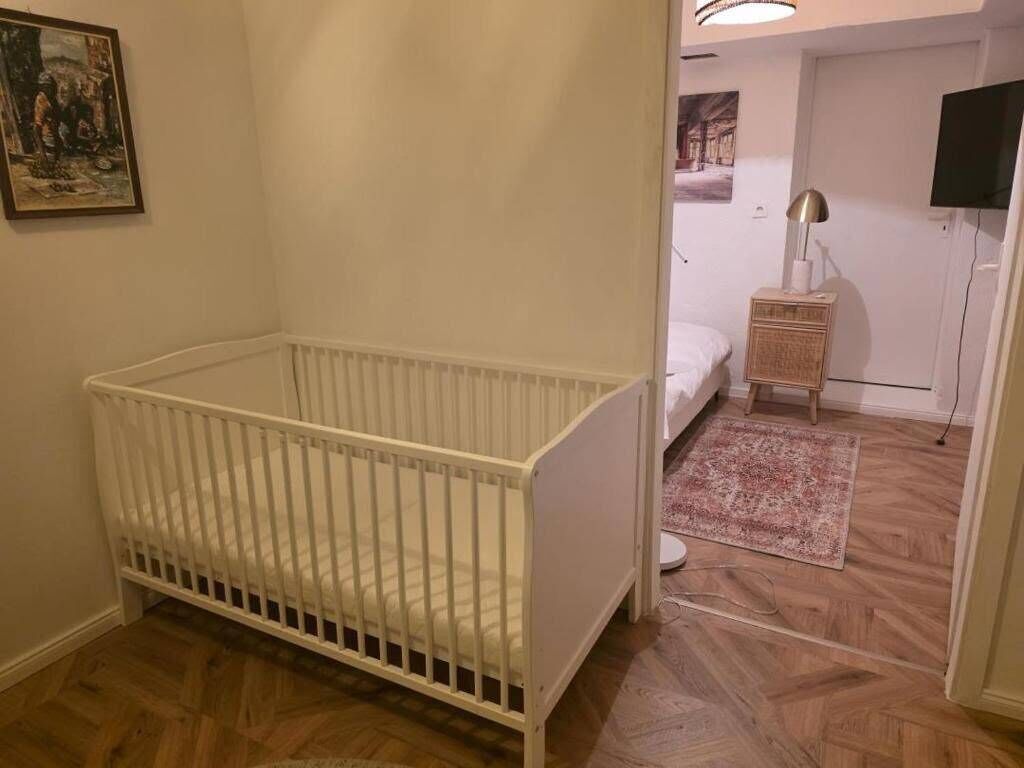 Huoneessa on valkoinen vauvansänky, pieni yöpöytä, lamppu ja seinälle asennettu televisio.