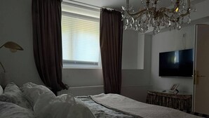 A bedroom with a bed, a television, a chandelier, and a window with curtains. - Stylish living in a 95-square-meter apartment with a great view from the garden (Bad Laasphe)